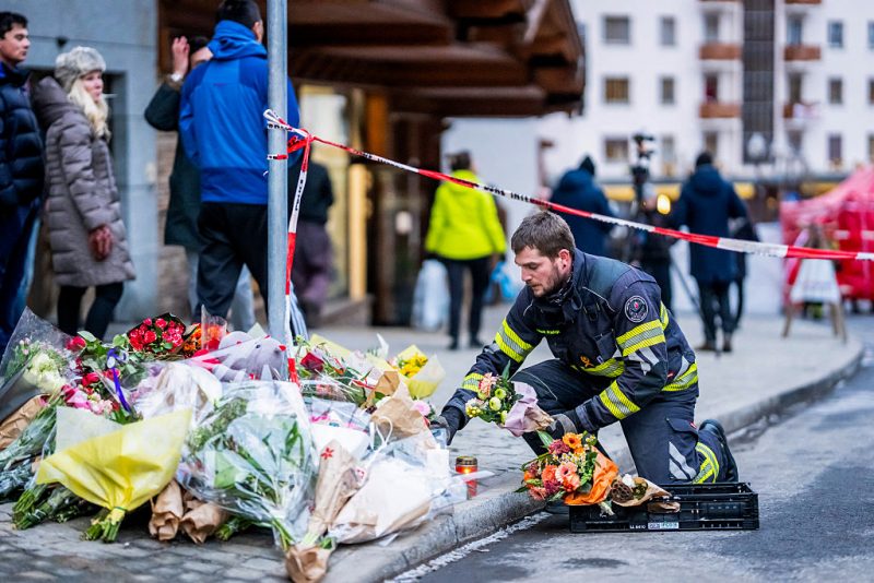 A firefighter displays flowers at a makeshift memorial near the site of a fire that ripped through a bar during New Year's Eve celebrations in the Alpine ski resort town of Crans-Montana killing around 40 people and injuring more than 100 others, in Crans-Montana on January 2, 2026. Investigators raced on January 2, 2026 to identify the victims of a fire that ripped through a bar in the Swiss Alps town of Crans-Montana, turning a New Year's celebration into one of the country's worst tragedies. Frederic Gisler, police commander in the Wallis canton in southwestern Switzerland, told reporters that authorities had counted "around 40 people who have died and around 115 injured, most of them seriously". (Photo by MAXIME SCHMID / AFP via Getty Images)