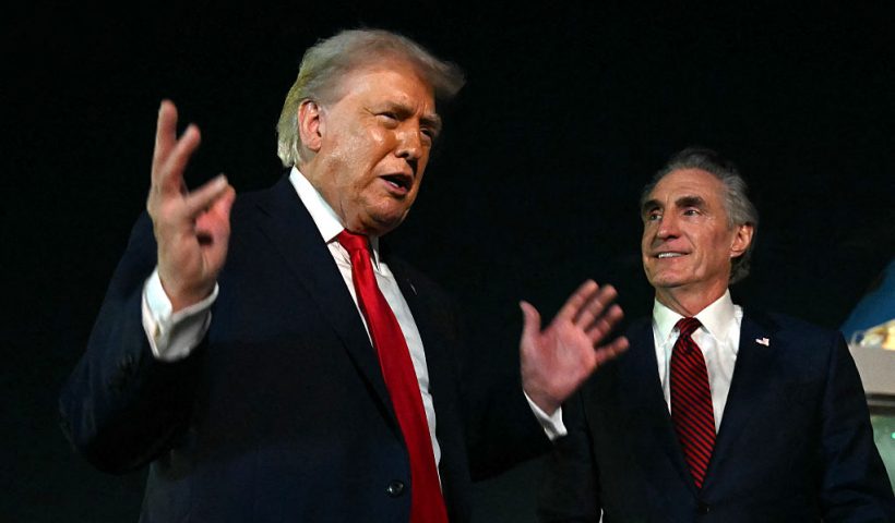 US President Donald Trump speaks with reporters as the Secretary of the Interior Doug Burgum (R) looks on, before boarding Air Force One at Palm Beach International Airport, in West Palm Beach, Florida on January 19, 2026. President Trump is returning to Washington after spending the weekend at his Mar-a-Lago residence and attending the College Football National Championship Game between Miami Hurricanes and Indiana Hoosiers at Hard Rock Stadium in Miami Gardens, Florida. (Photo by ANDREW CABALLERO-REYNOLDS / AFP via Getty Images)