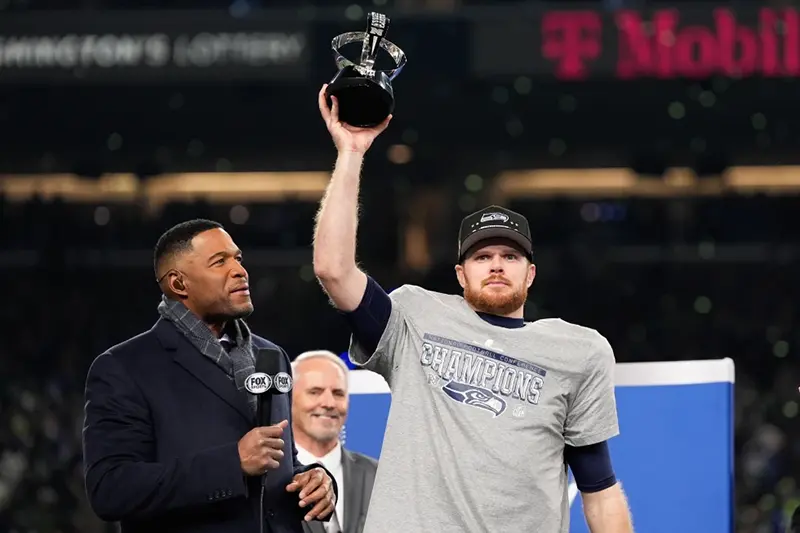 Seattle Seahawks quarterback Sam Darnold lifts the winner’s trophy next to Michael Strahan, left, after a win over the Los Angeles Rams in the NFC Championship NFL football game Sunday, Jan. 25, 2026, in Seattle. (AP Photo/Godofredo A. Vásquez)